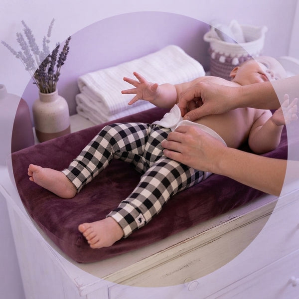 Close-up of soft bamboo bison plaid leggings showing fabric texture during a diaper change in a modern nursery.