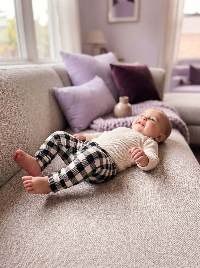A baby wearing bison plaid bamboo leggings relaxing on a comfortable sofa in a modern, stylishly decorated home.